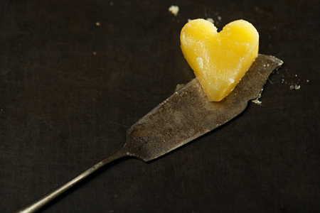 ghee or melted butter in heart shape on knife and dark metal backdropの写真素材