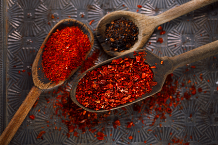 red hot chillies pepper flakes in vintage wooden spoons on textured metal backgroundの写真素材
