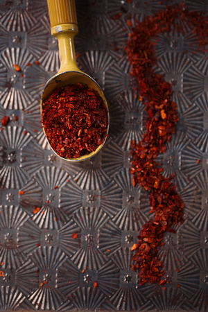 red hot chillies pepper flakes in vintage ice-cram spoon on textured metal backgroundの写真素材