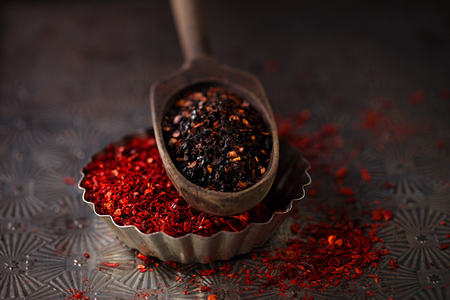 red hot chillies pepper flakes in vintage wooden spoons on textured metal backgroundの写真素材