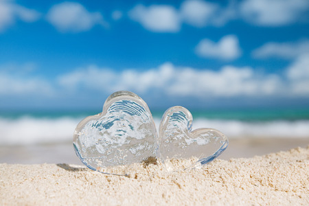 two clear glass hearts on white sand beach, ocean,  sky and seascapeの写真素材