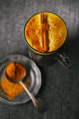 Turmeric latte or golden milk with cinnamon stick and spice mix, The drink is made by steaming milk with aromatic turmeric powder and spicesの写真素材
