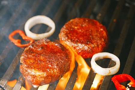 beef burgers spiced by berber rub with pepper and onion on bbq grill with flameの写真素材