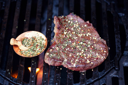 ribeye rib eye roast beef steak on bbq barbecue grill with flame and garlic chilli spice mix. Shallow dof.の写真素材