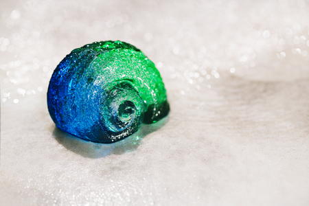 large blue green glass sea shell on white sand under water dropletsの写真素材