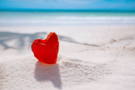 red heart shaped sea glass on white sand beach with seascapeの写真素材