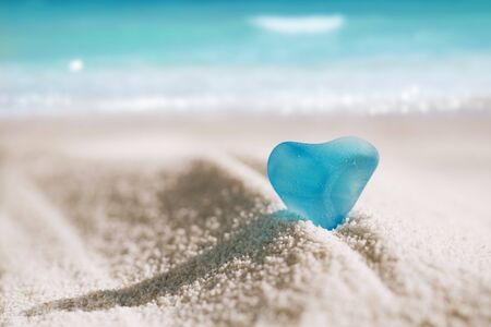 sea glass blue heart on white sand beach with seascapeの写真素材