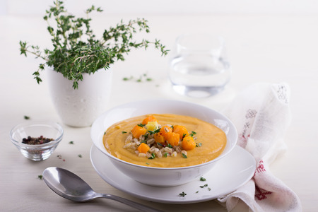 Vegetable cream soup with pumpkin and barley on a white tableの写真素材