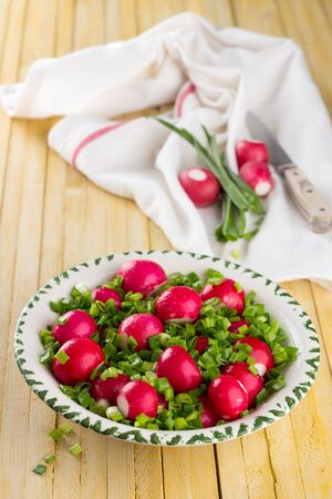 Bowl of red radishes and green onions on a wooden backgroundの写真素材