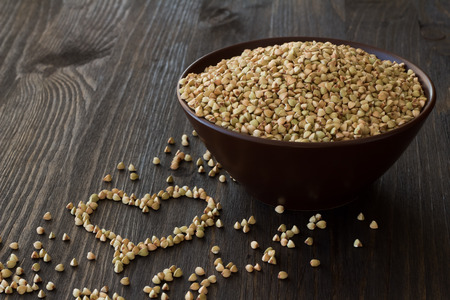 Green and brown buckwheat in ceramic bowl on a wooden surfaceの写真素材
