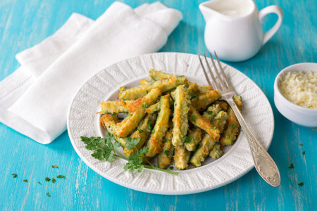 Baked zucchini in cheese batter with parsley, cheese and yogurt sauce on turquoise wooden table,...