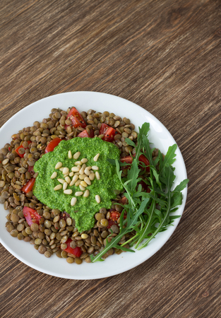 Homemade lentils with tomatoes and pesto sauce from arugula on a wooden background. Delicious healthy foodの写真素材