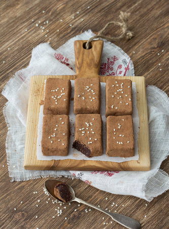 Chocolate sweets with dried fruits and sesame seeds on a wooden board on a wooden table, rustic...