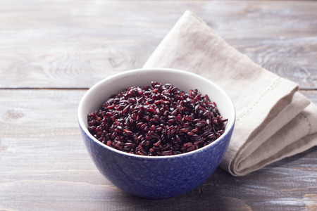 Black rice in a blue bowl on a wooden table, selective focus, rustic style. Simple healthy foodの写真素材