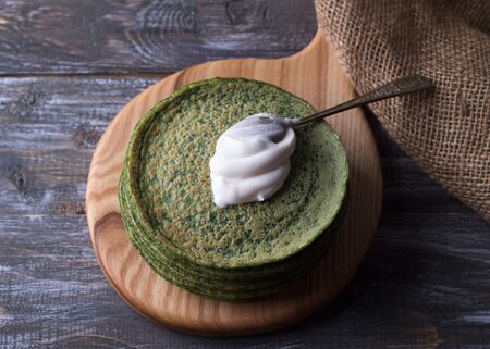 Stack of spinach pancakes with a spoon of sour cream on a wooden board on a wooden table, rustic style, selective focus. Simple healthy delicious foodの写真素材