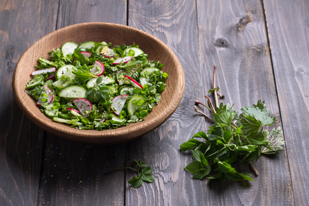 Vitamin salad of wild herbs with cucumber, radish and green onions in a wooden bowl on a wooden background, free space. Healthy detox diet foodの写真素材