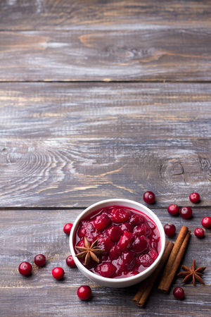 Homemade spicy cranberry sauce with fresh cranberries, cinnamon and star anise on a wooden background, top view, free spaceの写真素材