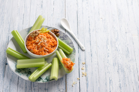 Delicious vegetable diet snack, celery stalks with carrot dip with nuts, garlic, spices and yoghurt dressing on light blue background, top view, selective focusの写真素材