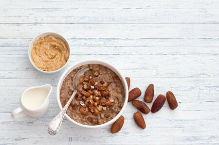Delicious oatmeal in a white bowl, dates fruits, cocoa and vegan milk. healthy breakfast on light blue background. top view. free spaceの写真素材