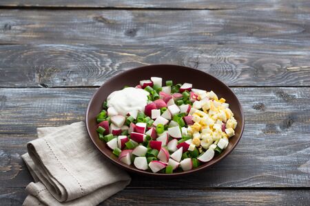 Fresh radish salad with green onions, boiled egg and sour cream on a wooden background, rustic style. Delicious homemade foodの写真素材
