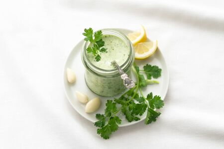 Yoghurt cilantro sauce with garlic and olive oil in a glass jar on a white background, selective focusの写真素材