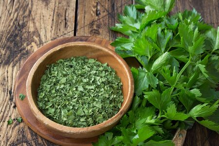Dried green celery in a wooden bowl and fresh celery on a wooden table, top viewの写真素材