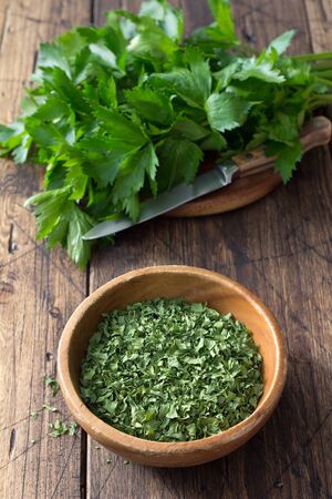 Dried green celery in a wooden bowl and fresh celery on a wooden table, top viewの写真素材