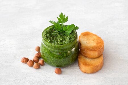 Fresh homemade parsley pesto with hazelnuts in glass jar and bread on light gray background. delicious vegan foodの写真素材