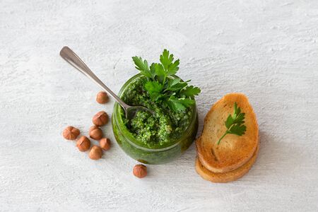Fresh homemade parsley pesto with hazelnuts in glass jar and bread on light gray background. delicious vegan foodの写真素材