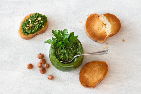 Fresh homemade parsley pesto with hazelnuts in glass jar and bread on light gray background. delicious vegan foodの写真素材