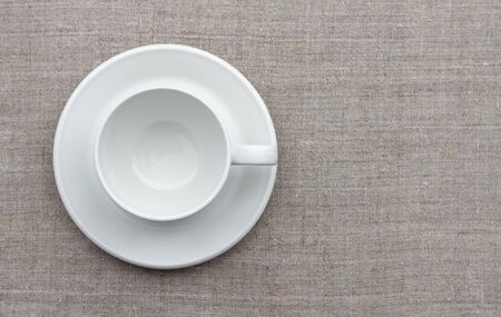 White cup and saucer on natural linen fabric, top view, free spaceの写真素材