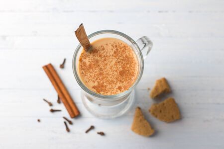 Spicy warming tea with milk in a glass cup and cinnamon sticks, cloves, with gingerbread cookie on light gray blue backgroundの写真素材