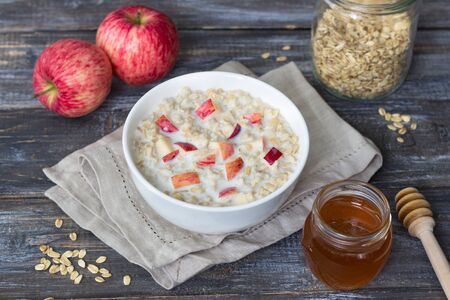 Milk oatmeal porridge with apple and honey in white bowl on wooden table. delicious healthy homemade breakfastの写真素材