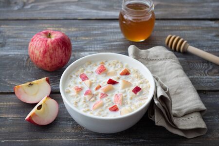 Milk oatmeal porridge with apple and honey in white bowl on wooden table. delicious healthy homemade breakfastの写真素材
