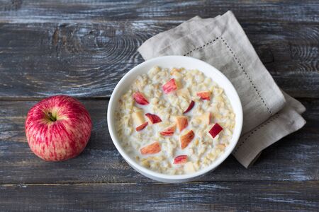 Milk oatmeal porridge with apple and honey in white bowl on wooden table. delicious healthy homemade breakfastの写真素材