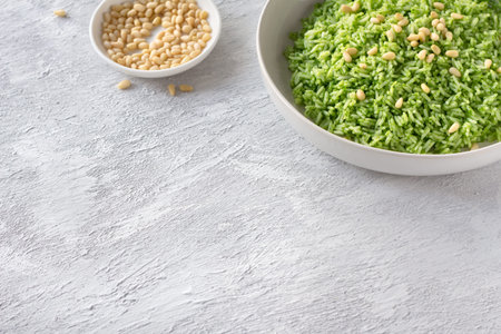 Vegan rice with green oil and pine nuts in a white bowl on a gray background, free space. delicious...