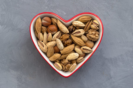 Variety of nuts in red bowl heart shaped on gray background. almonds, walnuts, hazelnuts,...