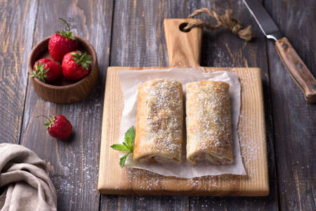 Sweet Mexican chimichanga with banana and strawberries, sprinkled with powdered sugar on a wooden table. top view. spaceの写真素材
