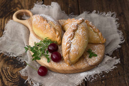 Sweet homemade baked mini pies with cherry and cinnamon on wooden background, selective focusの写真素材