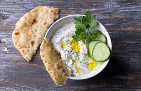 Traditional greek yogurt tzatziki sauce with cucumbers and herbs on wooden background, top view, spaceの写真素材