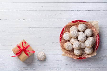 Christmas homemade gingerbread cookies sprinkled with powdered sugar on red plate on light blue background with gift wrapped in craft paper with red ribbon, flat lay, free spaceの写真素材