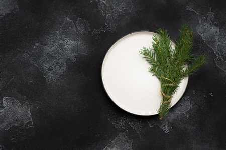 Branch of a natural Christmas tree wrapped in gold wire on a white plate. Dark textured background, top view, copy space. New Year or Christmas decorの写真素材