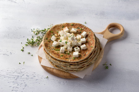 Homemade yeast-free gluten-free buckwheat flat bread with feta cheese, thyme and spices on a wooden board, light blue textured background. Healthy food conceptの写真素材