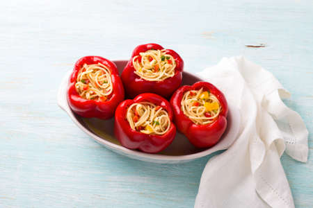 Bell red peppers stuffed with spaghetti, vegetables, cheese and herbs in the form before baking on a light blue background, top view. Stuffed peppers cooking process, homemade foodの写真素材