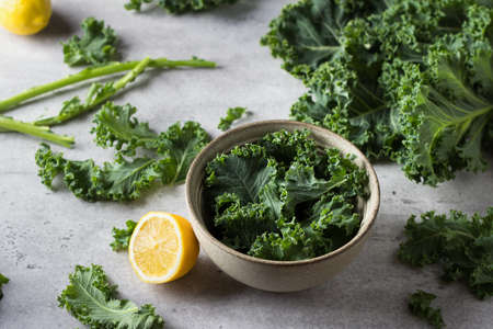 Fresh torned kale leaves in a bowl with lemon and whole kale leaves on gray textured background, top view. Cooking kale saladの写真素材