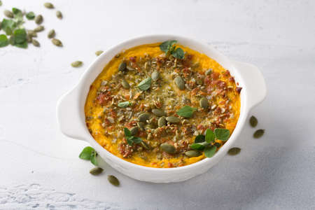 Homemade pumpkin casserole or gratin with cheese and pumpkin seeds in two ceramic tins on a light gray background, top view, free spaceの写真素材