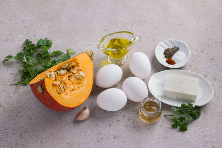 Ingredients for cooking scrambled eggs with pumpkin: fresh eggs, raw pumpkin, feta cheese, olive oil, apple cider vinegar, garlic, herbs and spices on a beige textured background, top viewの写真素材