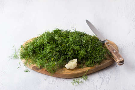 Wooden board of chopped dill with a knife on a light gray background. Cooking homemade foodの写真素材