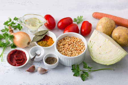 Ingredients for vegetable stew: peas, potatoes, cabbage, carrots, onions, garlic, tomatoes, vegetable oil, tomato paste, herbs, salt and spices on a light blue background. Cooking delicious vegan foodの写真素材