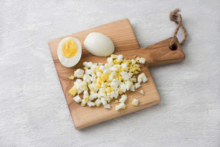 Wooden board with chopped eggs on a light gray background, top view. Preparing homemade saladの写真素材